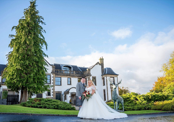 Bride and groom pose outside Gleddoch with deer statue in background